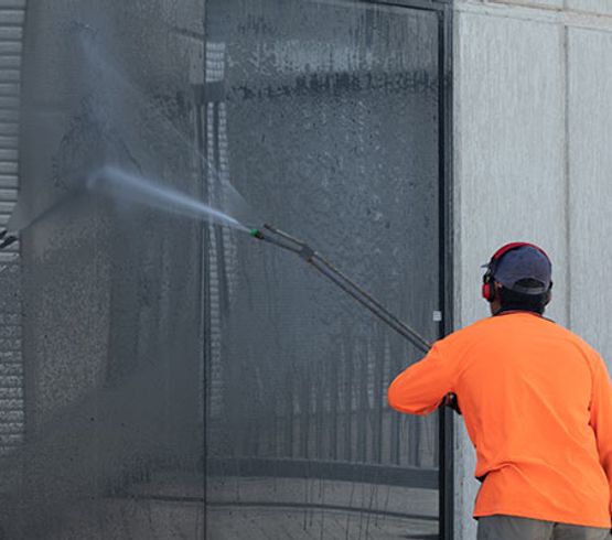 Professional worker cleaning commercial window with pressure washing equipment