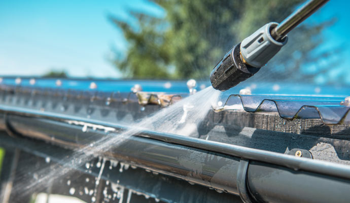 Person cleaning gutter with pressure washer