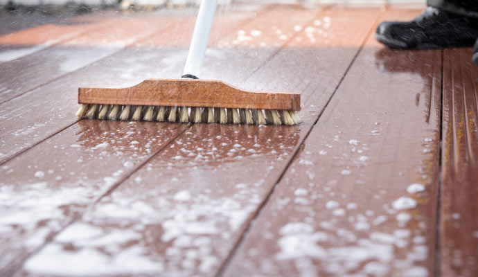 Person cleaning wooden deck with brush