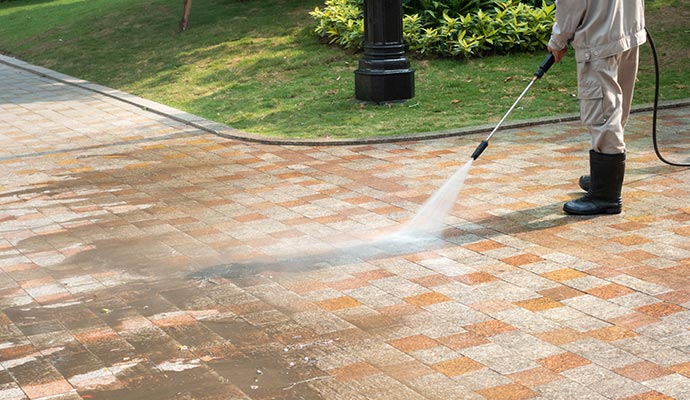 A person pressure washing a tiled pavement with equipment